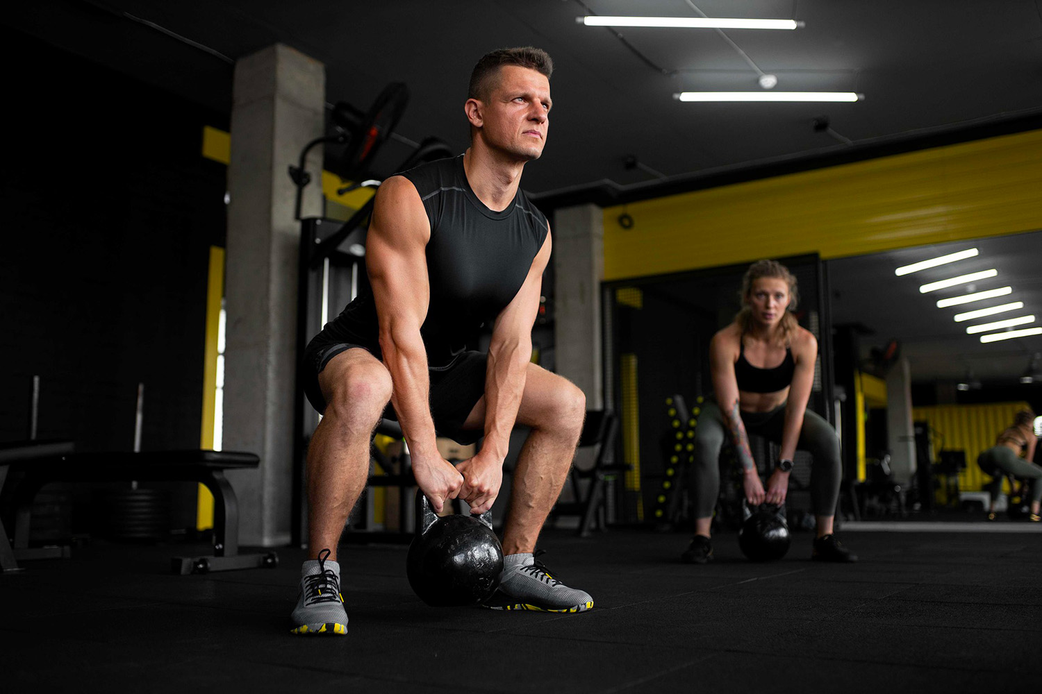 Uomo e donna si allenano con kettlebell in palestra, dopo trattamento di tricopigmentazione.